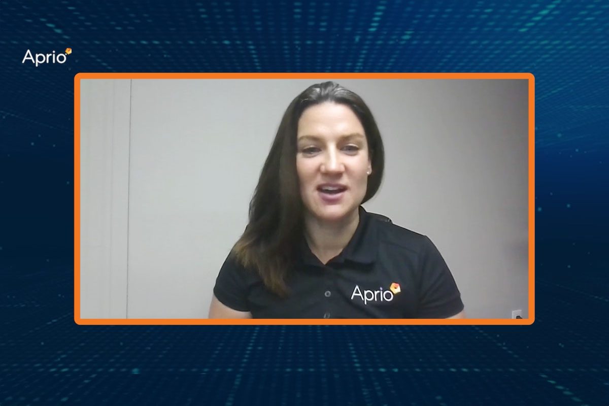 A woman wearing an Aprio-branded black polo shirt speaks on a video call, framed by an orange border with the Aprio logo in the top left corner.