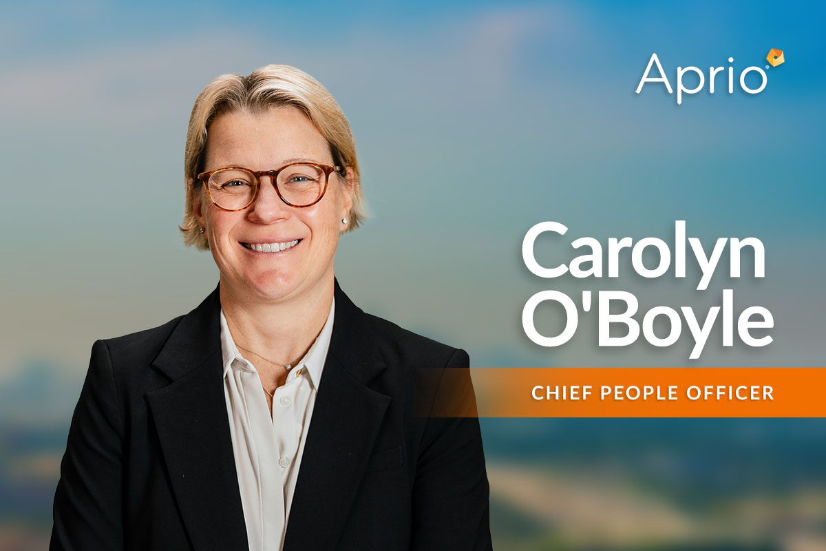 A person in a suit and glasses smiles at the camera with the text Aprio, Carolyn OBoyle, Chief People Officer displayed beside them on a blurred background.