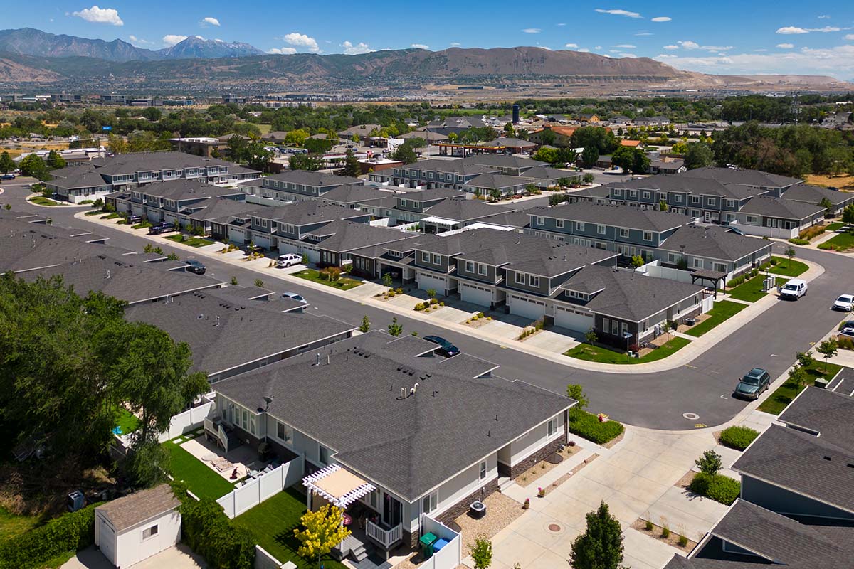 Aerial view of a suburban neighborhood with rows of modern houses, streets, and driveways, set against distant mountains under a clear sky.