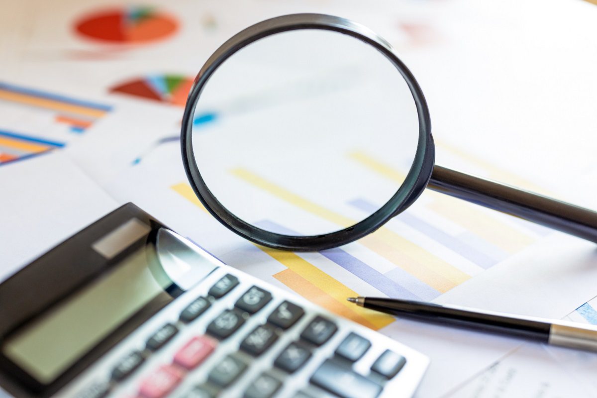 A magnifying glass, calculator, and pen rest on printed charts and graphs, suggesting financial analysis or data review.