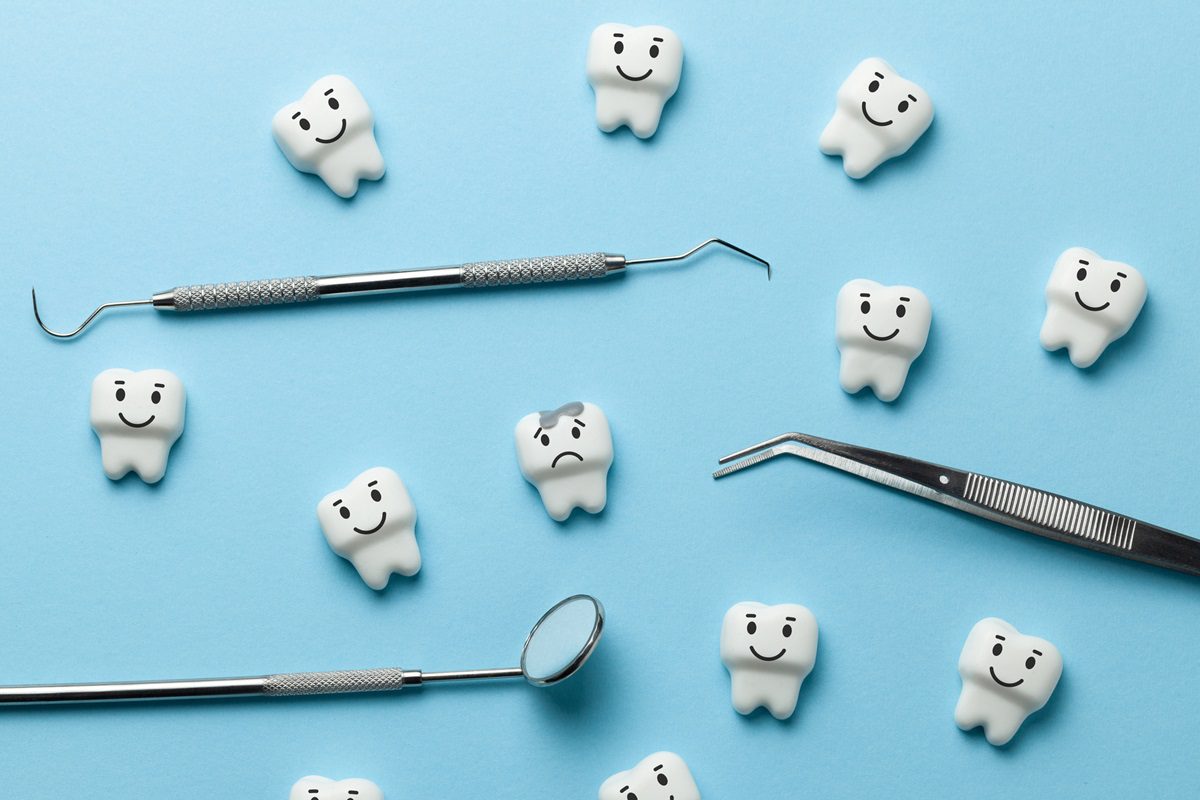 Dental tools and model teeth with happy faces, except one with a sad face and a visible cavity, displayed on a blue background.
