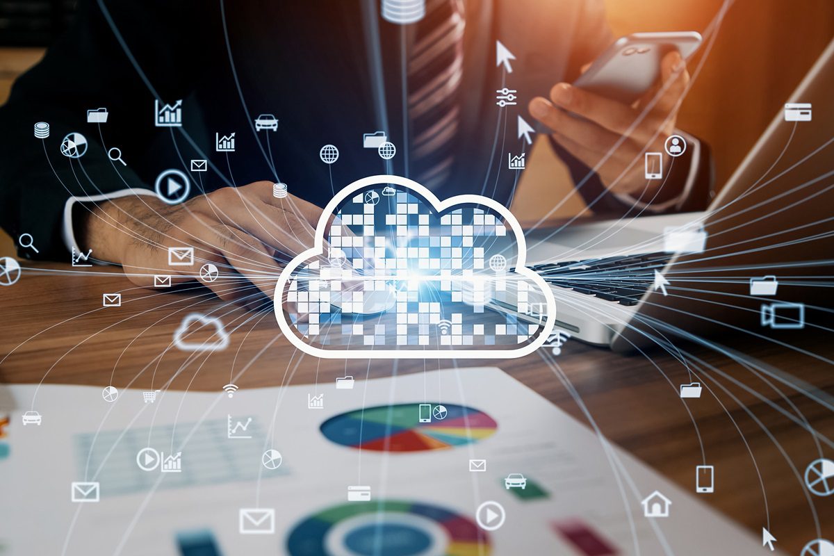 A person uses a smartphone and laptop at a desk with business charts, overlaid by a digital cloud icon and various technology and data symbols representing cloud computing.
