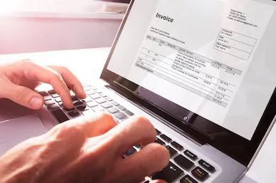 Hands typing on a laptop keyboard with an invoice document displayed on the screen.
