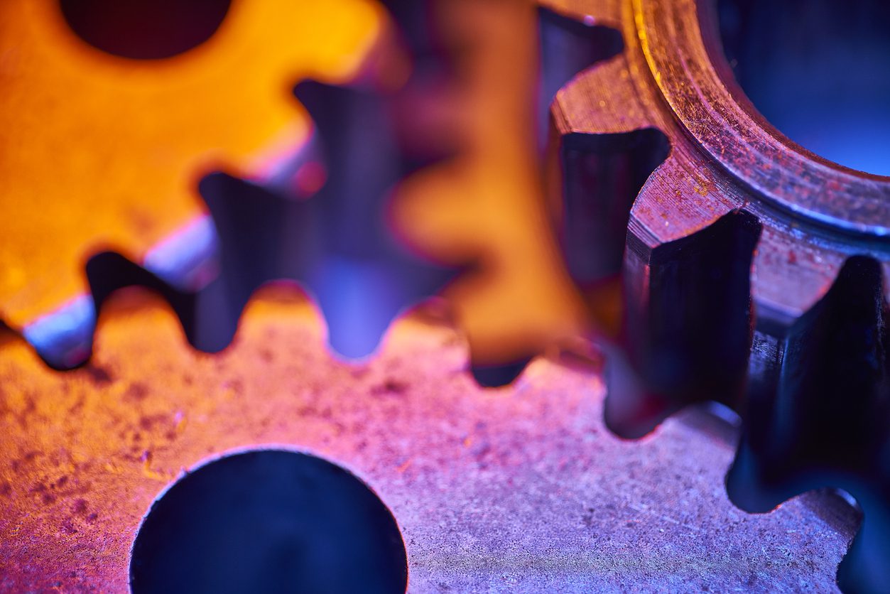 Close-up view of two interlocking metal gears with blue and orange lighting highlighting their textures and edges.