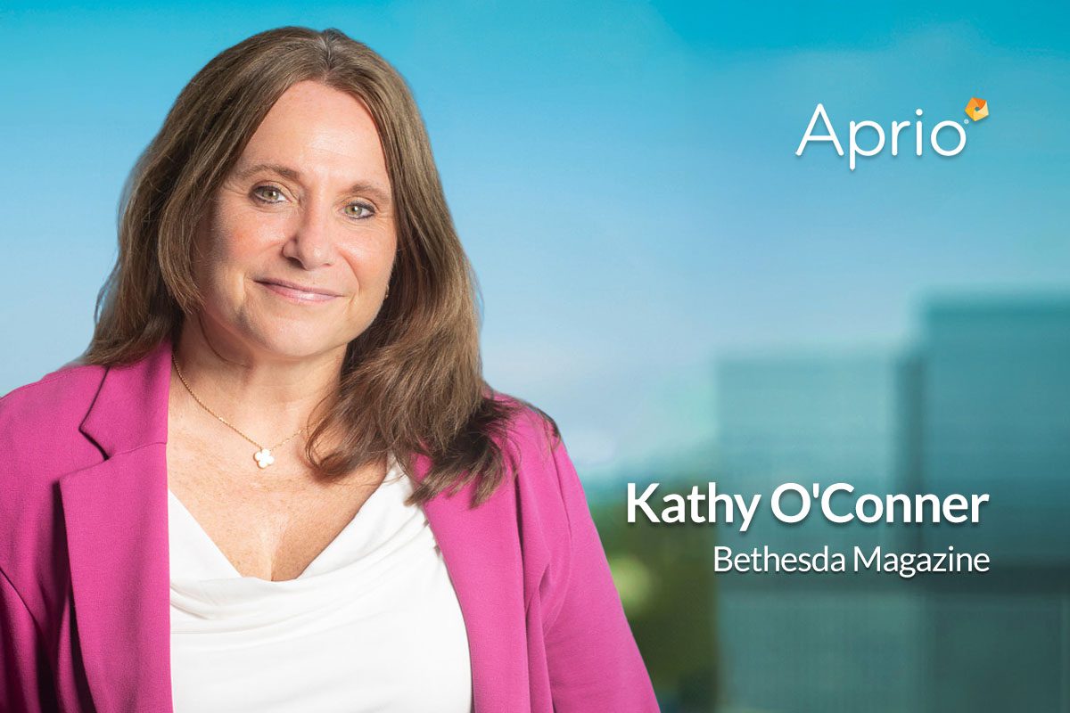A woman in a magenta blazer poses in front of a blurred cityscape background with the text Aprio, Kathy OConner, and Bethesda Magazine.