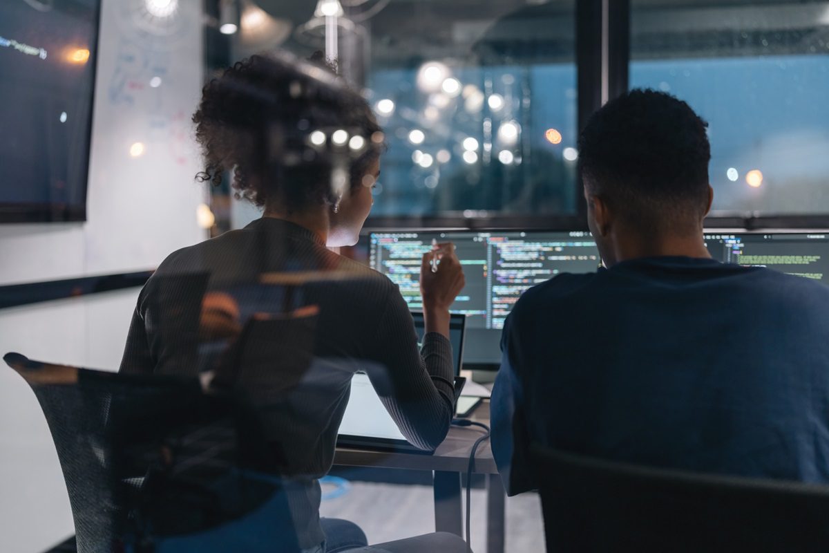 Two programmers working together on a computer code at night. Computer operators running system diagnostic tests. IT specialists deploying error checking utilities to fix network issues.