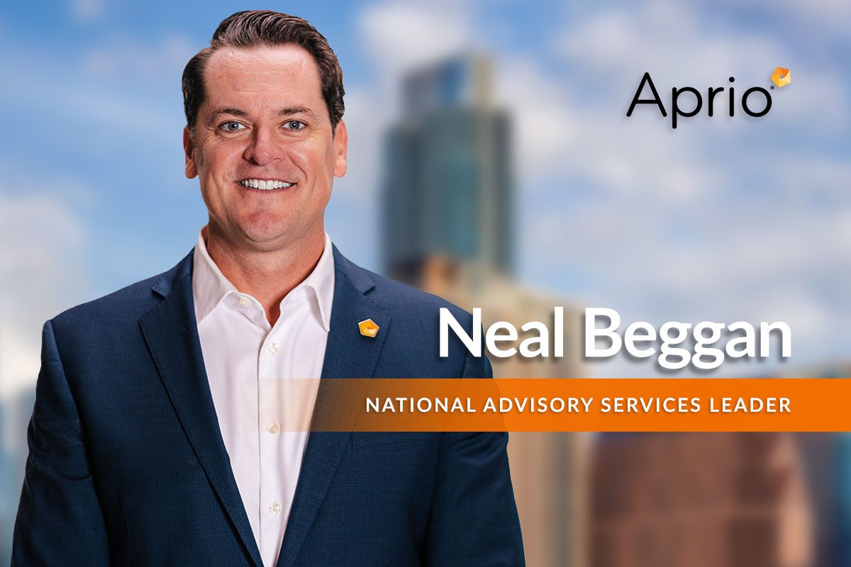 A man in a suit stands in front of a blurred cityscape background with the text Aprio, Neal Beggan, and National Advisory Services Leader displayed beside him.