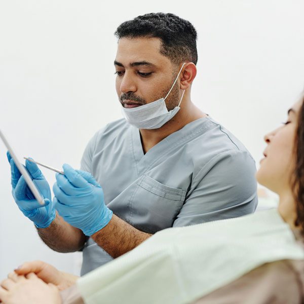 Male dentist with a face mask explains something to a female patient in a dental chair