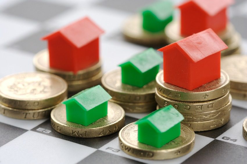 Plastic red and green house tokens are placed on stacks of British one pound coins on a chessboard, representing property investment or real estate strategy.