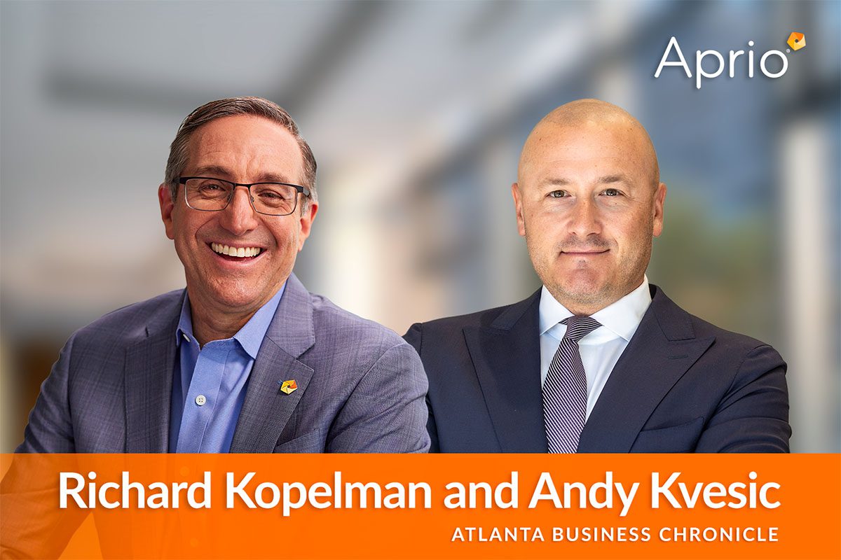 Two men in business attire, smiling, are pictured in front of a blurred office background with the Aprio logo and the names Richard Kopelman and Andy Kvesic, Atlanta Business Chronicle.
