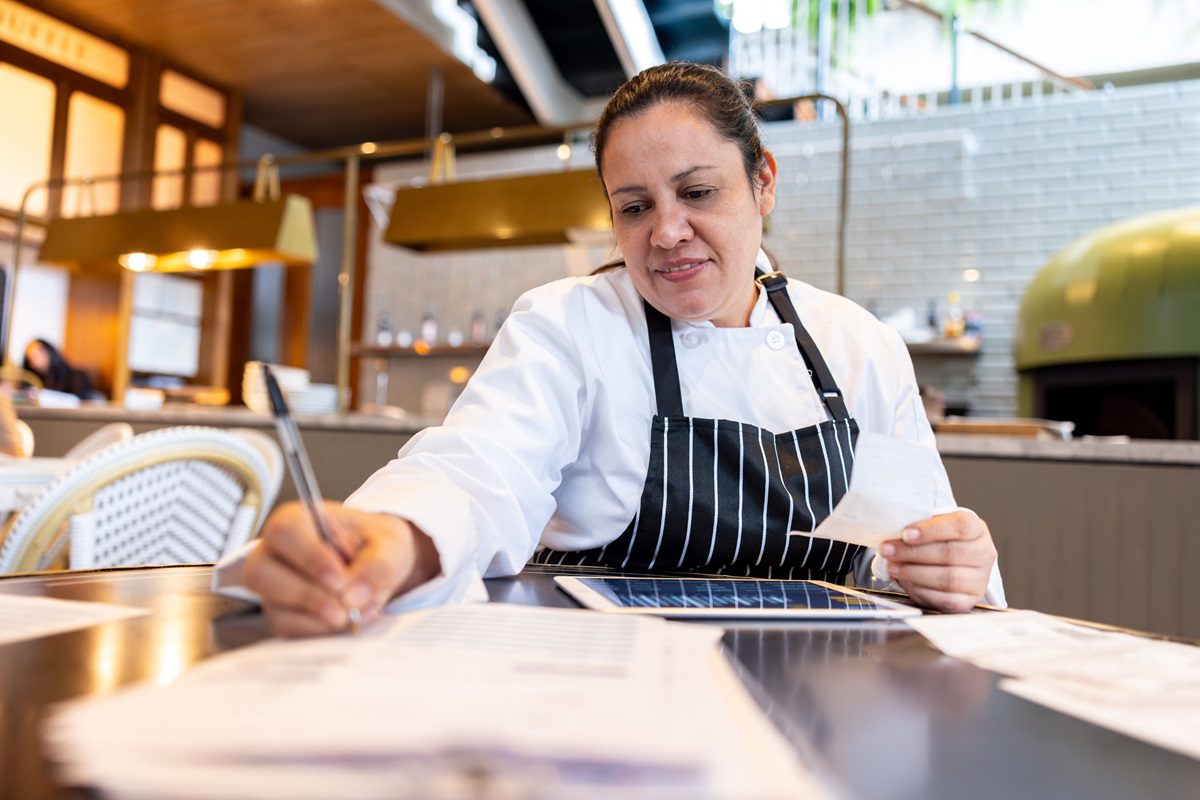 Latin American female chef doing the accountancy and looking at receipts at the restaurant - small business concepts