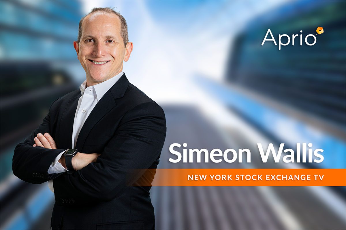A man in a suit stands smiling with arms crossed. Text reads Simeon Wallis and New York Stock Exchange TV. The Aprio logo is in the top right corner.