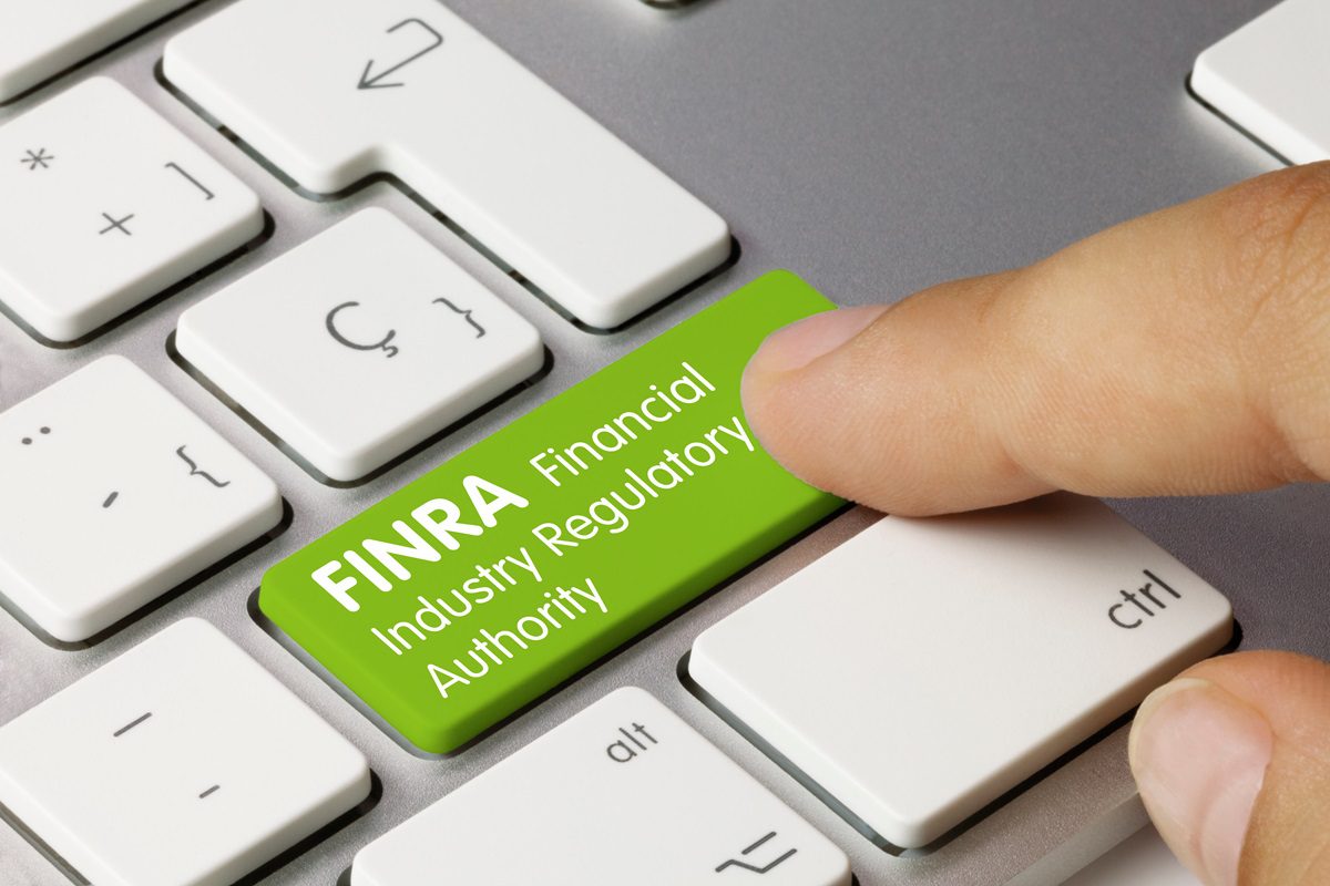 FINRA Financial Industry Regulatory Authority Written on Orange Key of Metallic Keyboard. Finger pressing key.