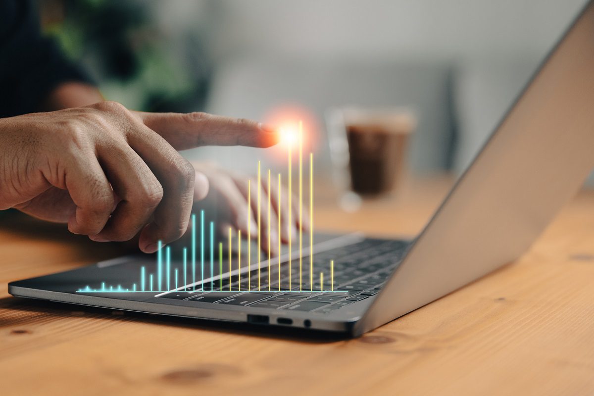 A person touches a laptop keyboard with digital bar graphs appearing above it, suggesting data analysis or interactive technology.