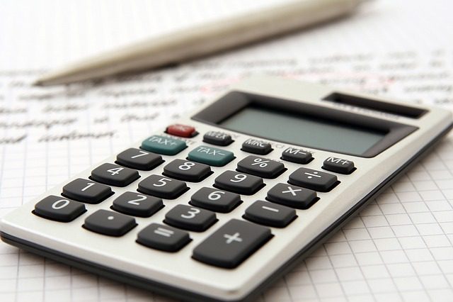 A calculator and pen rest on a sheet of graph paper with handwritten notes.