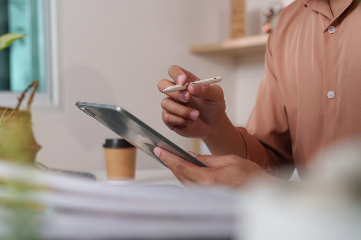 A young man utilizes a tablet and stylus for efficient note-taking, reflecting modern remote work practices in a comfortable setting.