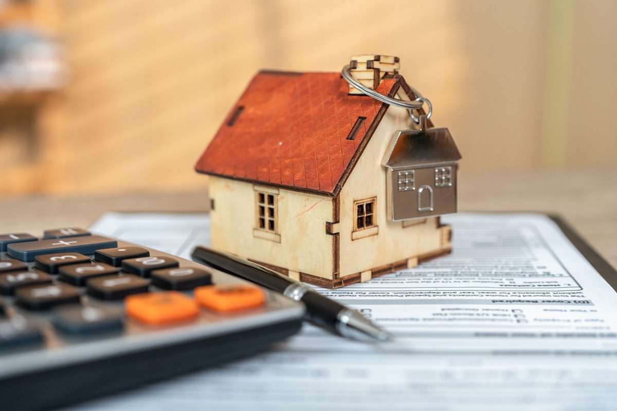 A small model house with a keychain, a pen, and a calculator are placed on top of a document with printed text.