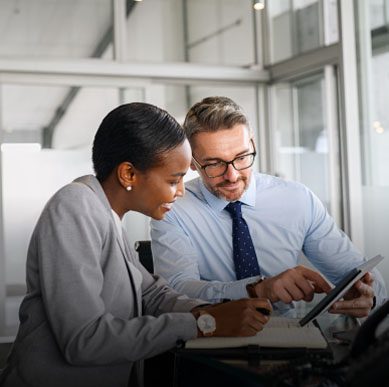 A man and woman sit in a sunny office and smile at something on a tablet