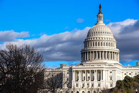 The United States Capitol building in Washington, D.C., with a clear blue sky and some clouds in the background.