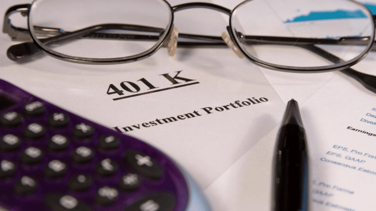 Close-up of a 401k investment portfolio document with a pair of eyeglasses, a pen, and a calculator resting on top.